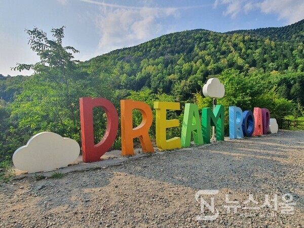 장복 하늘마루길에 조성된 DREAM ROAD 영문조형물. 안민도로를 걷다보면 우측으로 갈림길이 나오는데 이곳으로 진입하면 진해드림로드의 두 번째 길인 ‘장복 하늘마루길’로 접어들게 된다. ‘장복 하늘마루길’은 안민도로 안민휴게소에서 시작하여 삼밀사 옆 장복산 입구까지 연결된 약 4km 정도 길이의 걷기길로 안민도로에서 하늘마루까지는 약간 경사가 있는 오르막길을 계속 올라가야 한다. 장복 하늘마누길을 걷다보면 길 바깥쪽에 알파벳으로 되어있는 DREAM ROAD 영문조형물을 볼 수 있다.